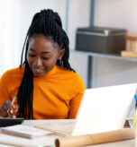 Close up of one African American woman using calculator, calculating finance at home, female hands and paper document at table close up, economist or financier writing report, student doing homework